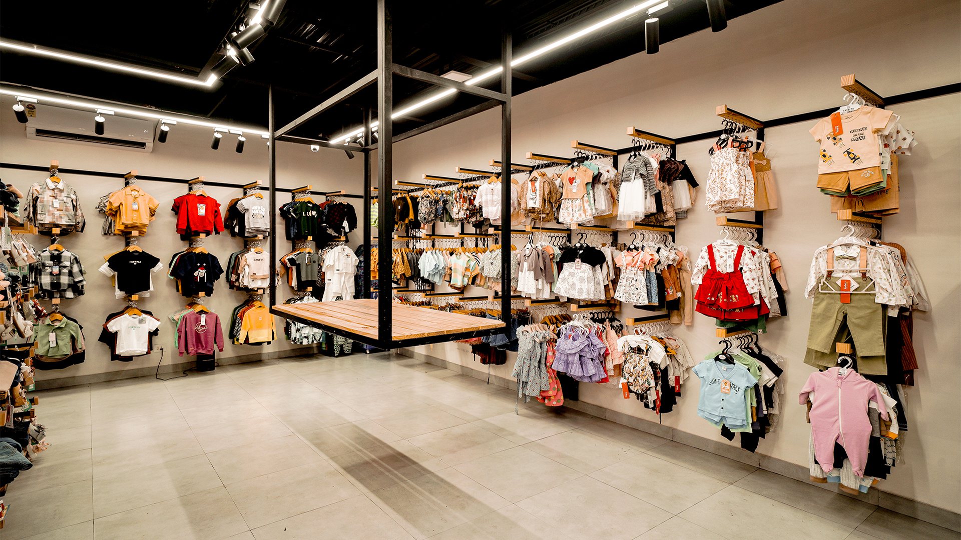 Open children's clothing floor with wall displays, wood tables and a black geometric lighting grid