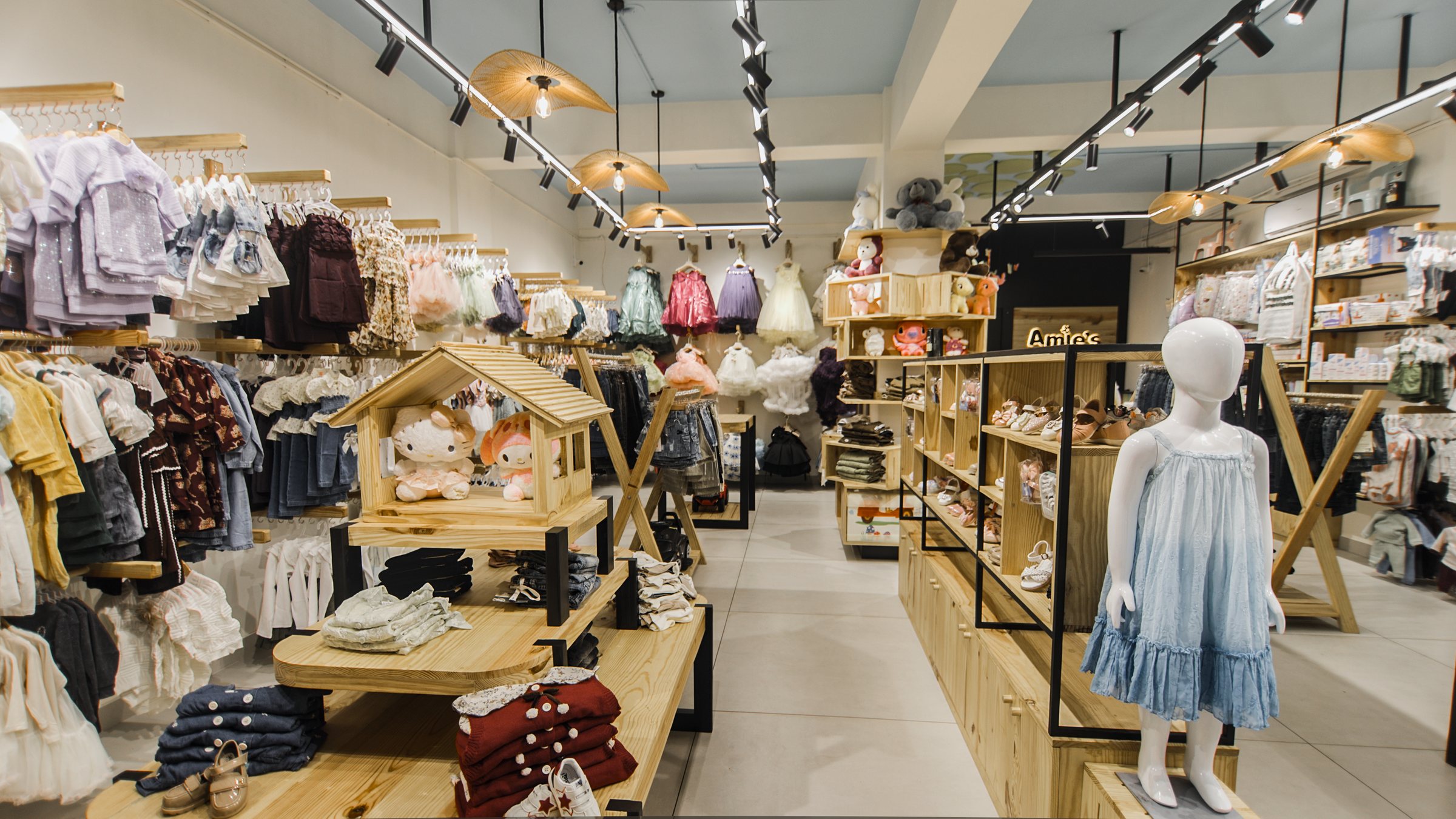 Full shop aisle with layered clothing displays, wood tables and warm pendant lights