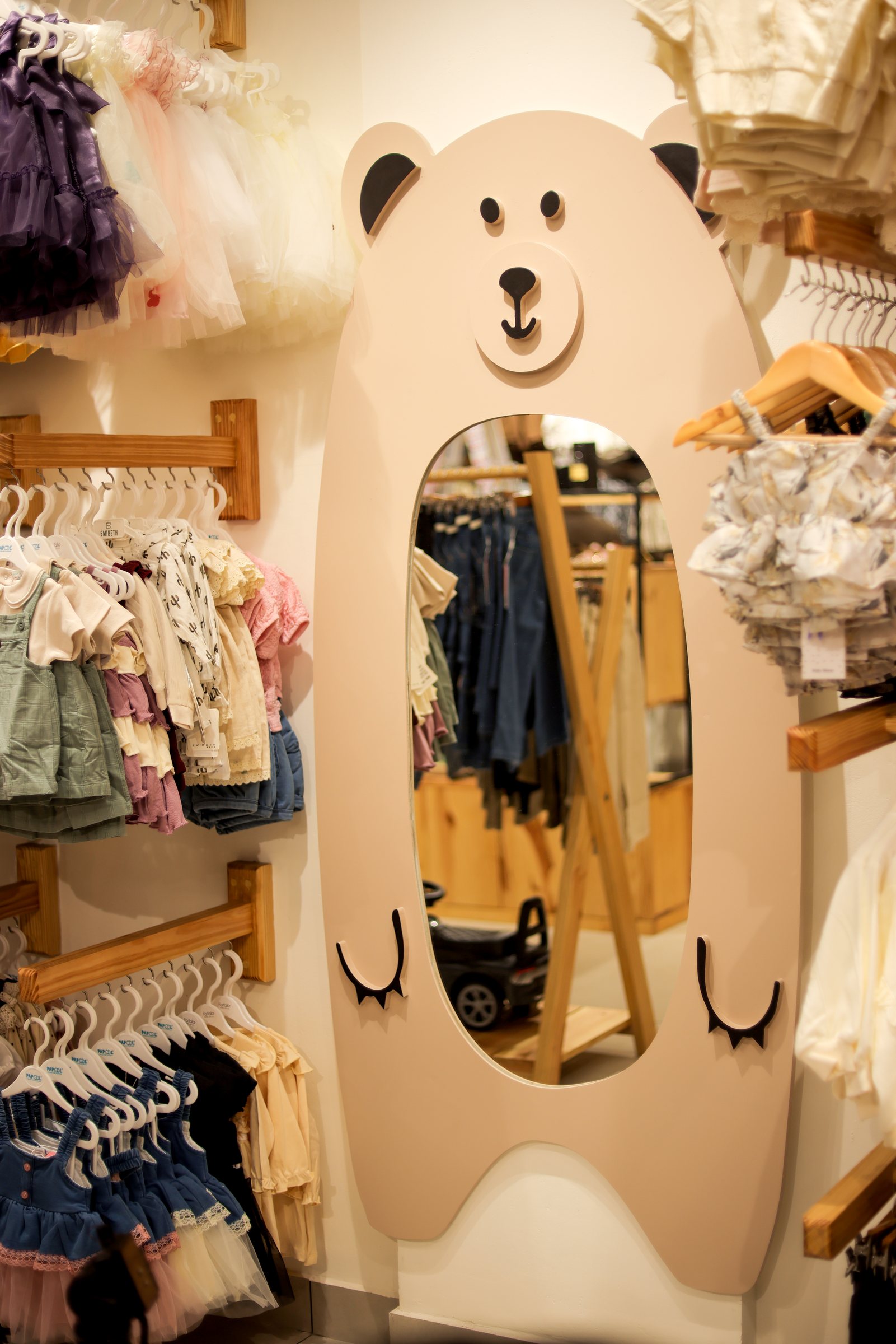 Bear-shaped floor mirror nestled between closely packed children's clothing racks