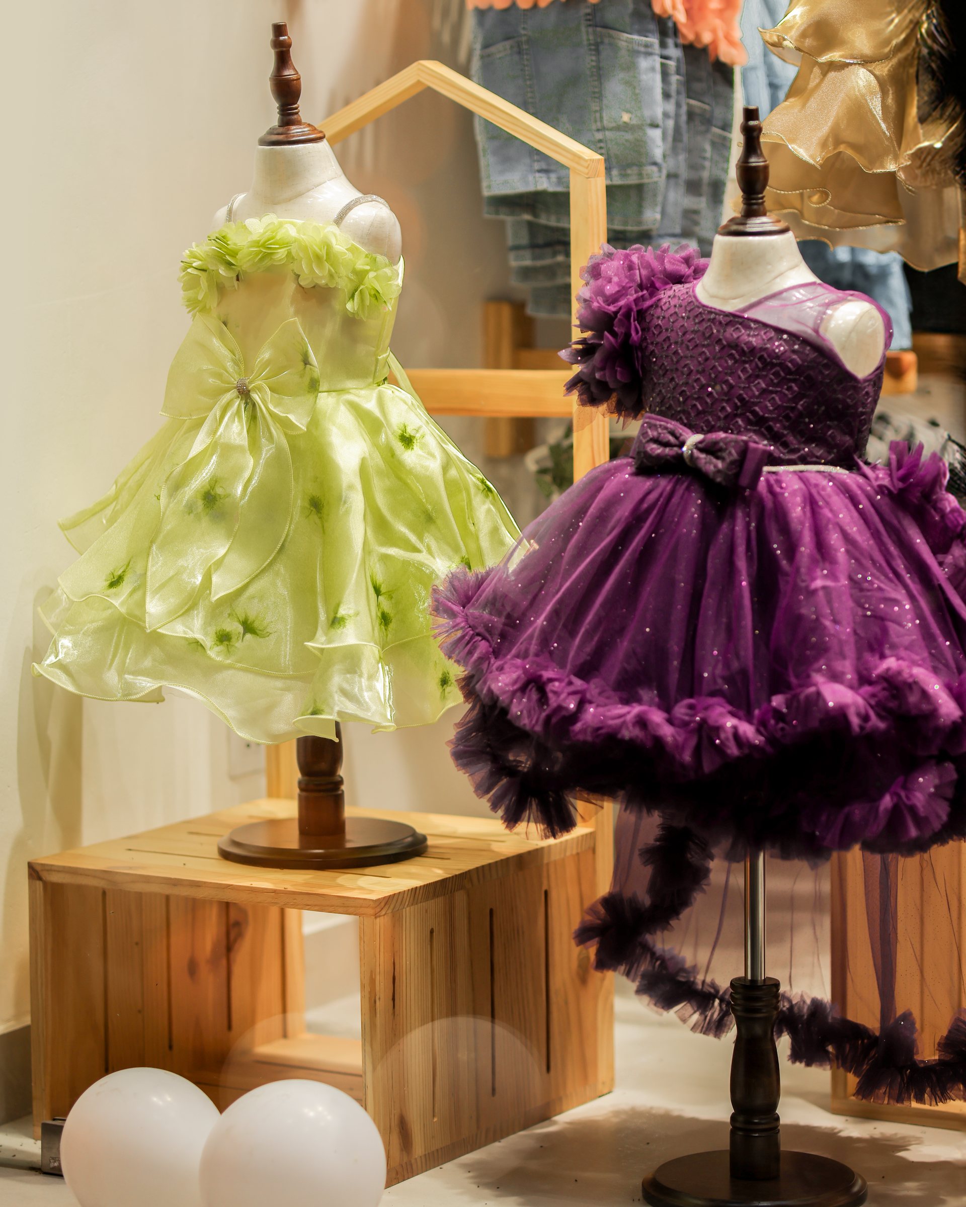 Green and purple party dresses on child mannequins beside stacked wood display boxes
