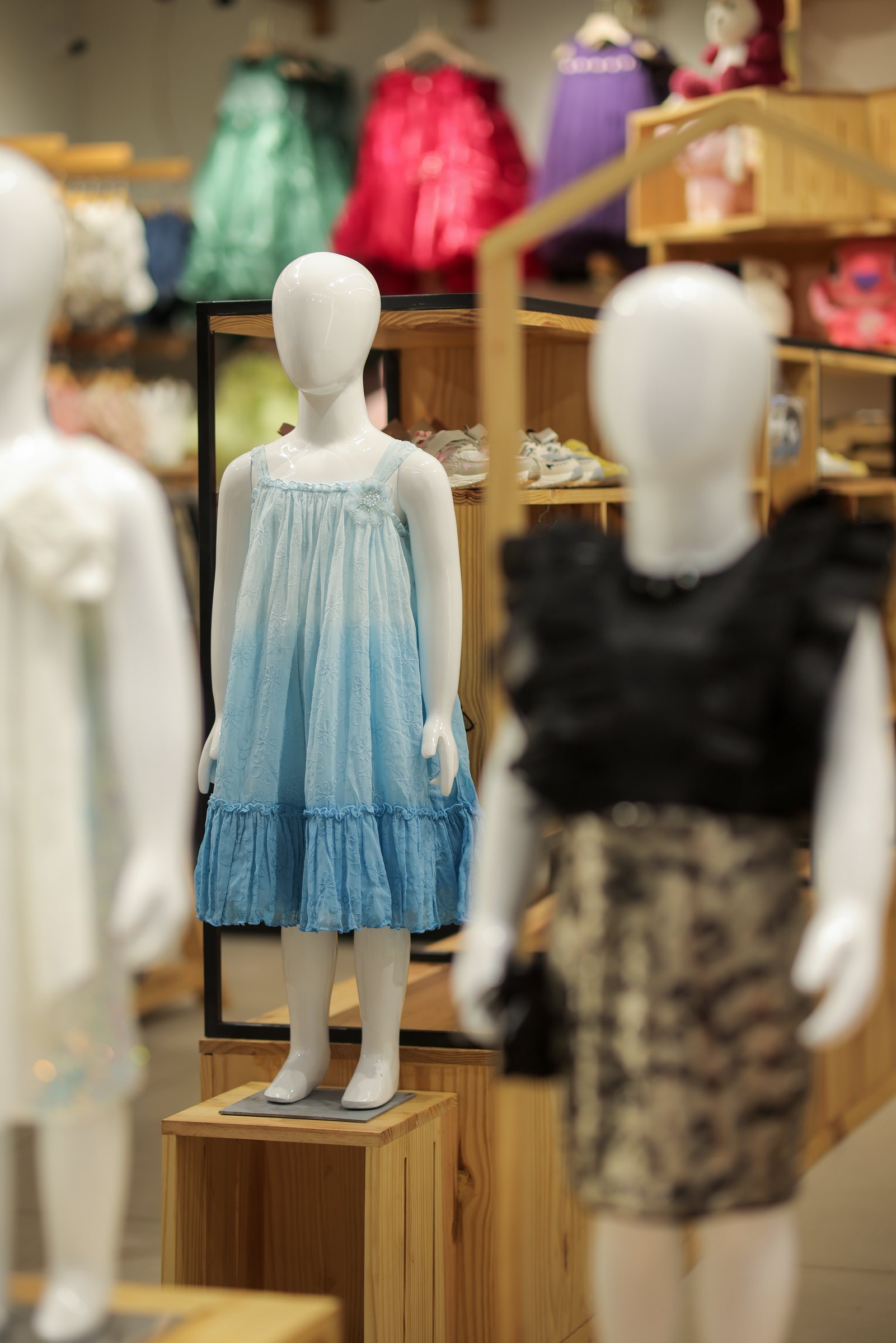 Child mannequin in a pale blue dress surrounded by softly focused clothing displays