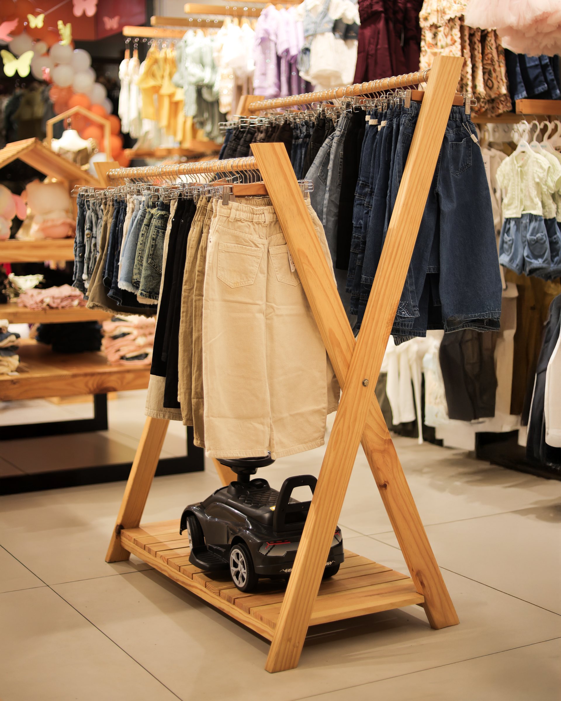 A-frame wood rack filled with children's trousers above a small ride-on car