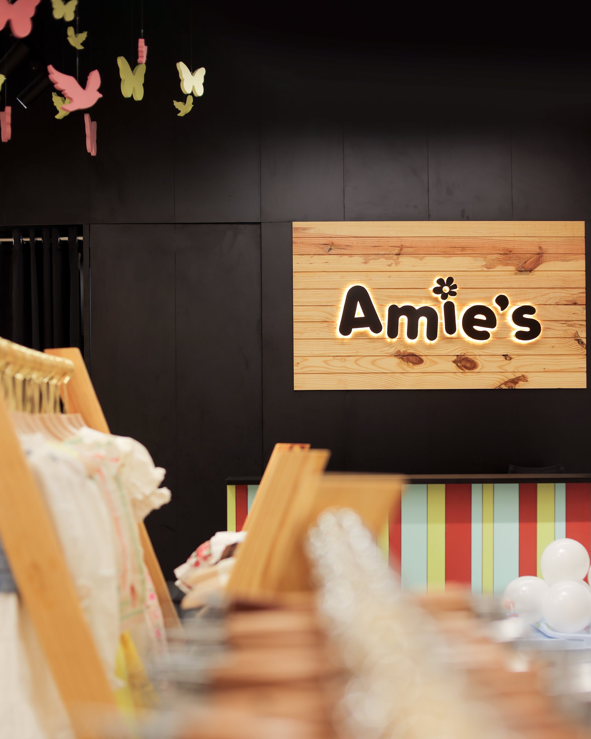 Wood Amie's sign on a black wall above striped paneling and blurred clothing displays