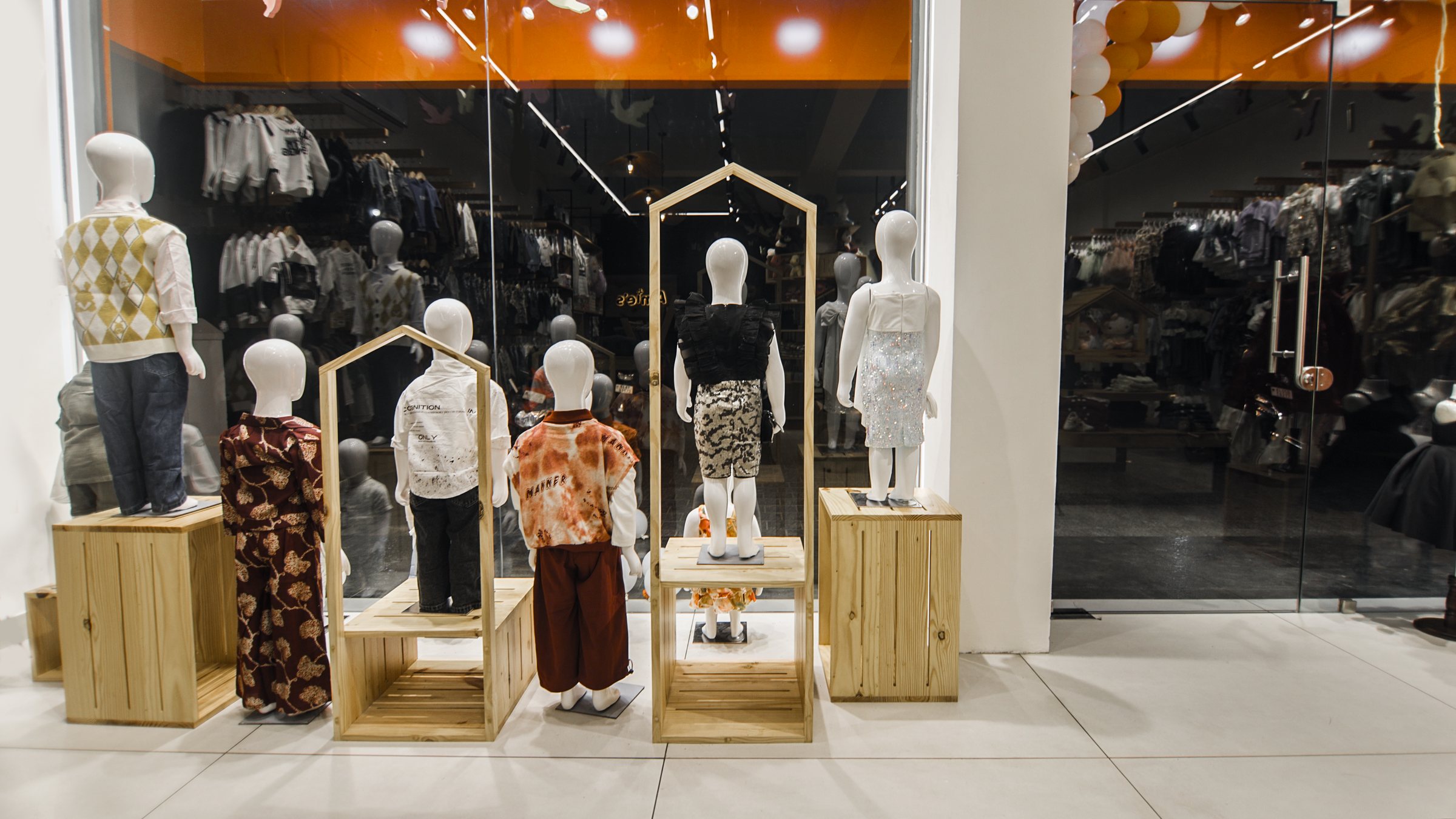 Children's mannequins arranged on wood platforms before a dark glazed storefront