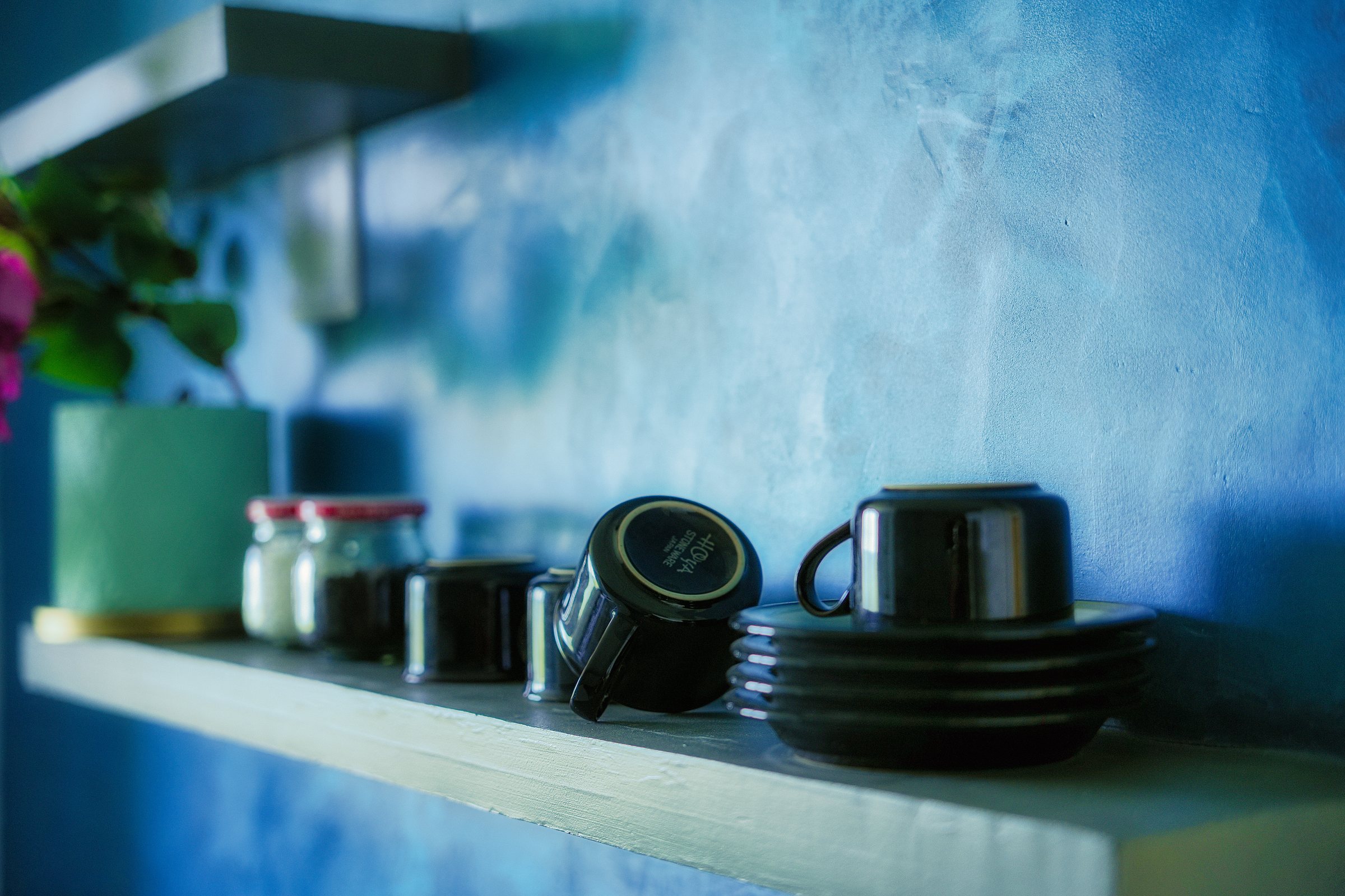 Close view of stacked black cups and saucers on a pale shelf against blue plaster