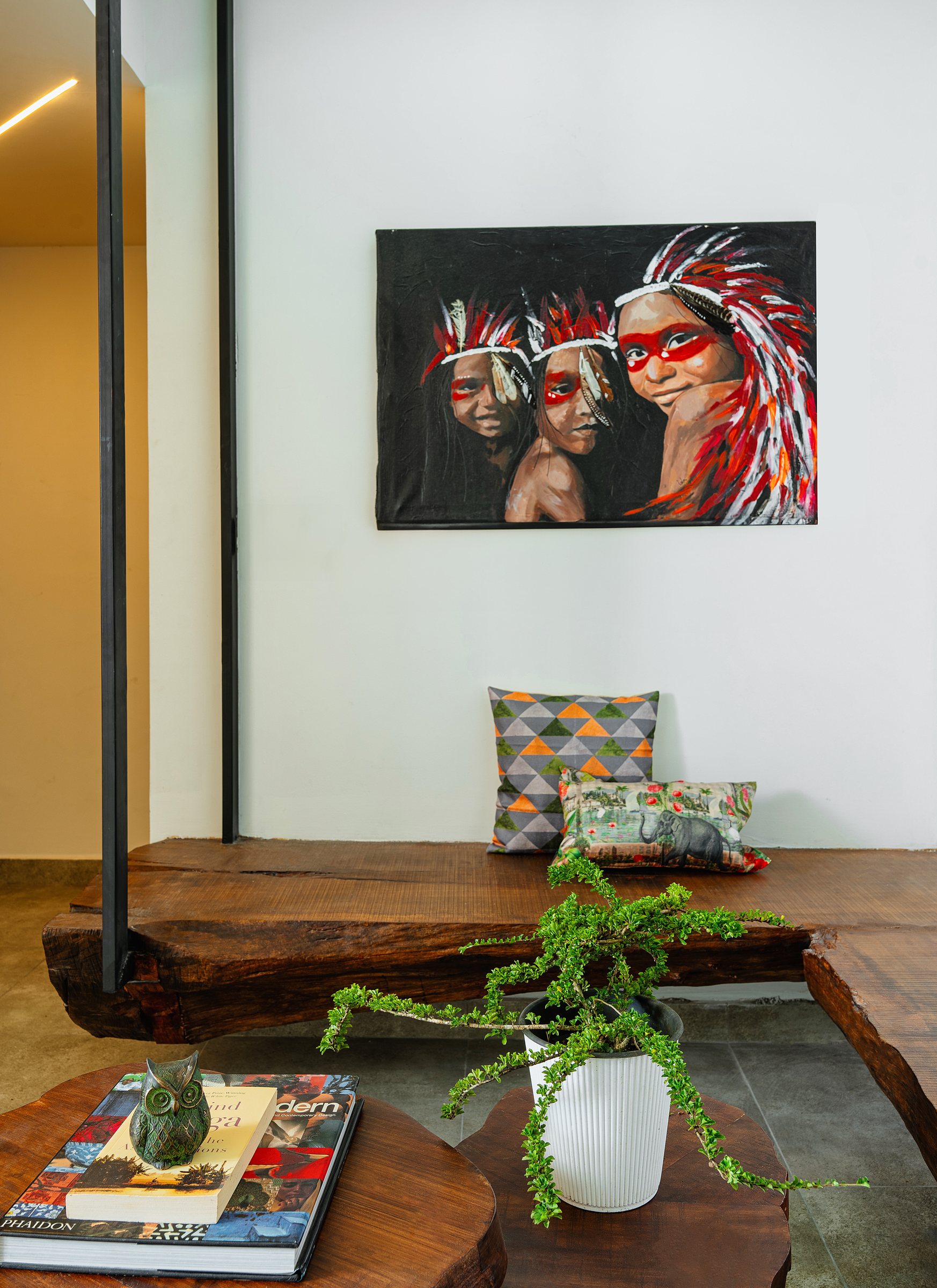 Patterned cushions and trailing foliage on a live-edge bench beneath bold figure artwork