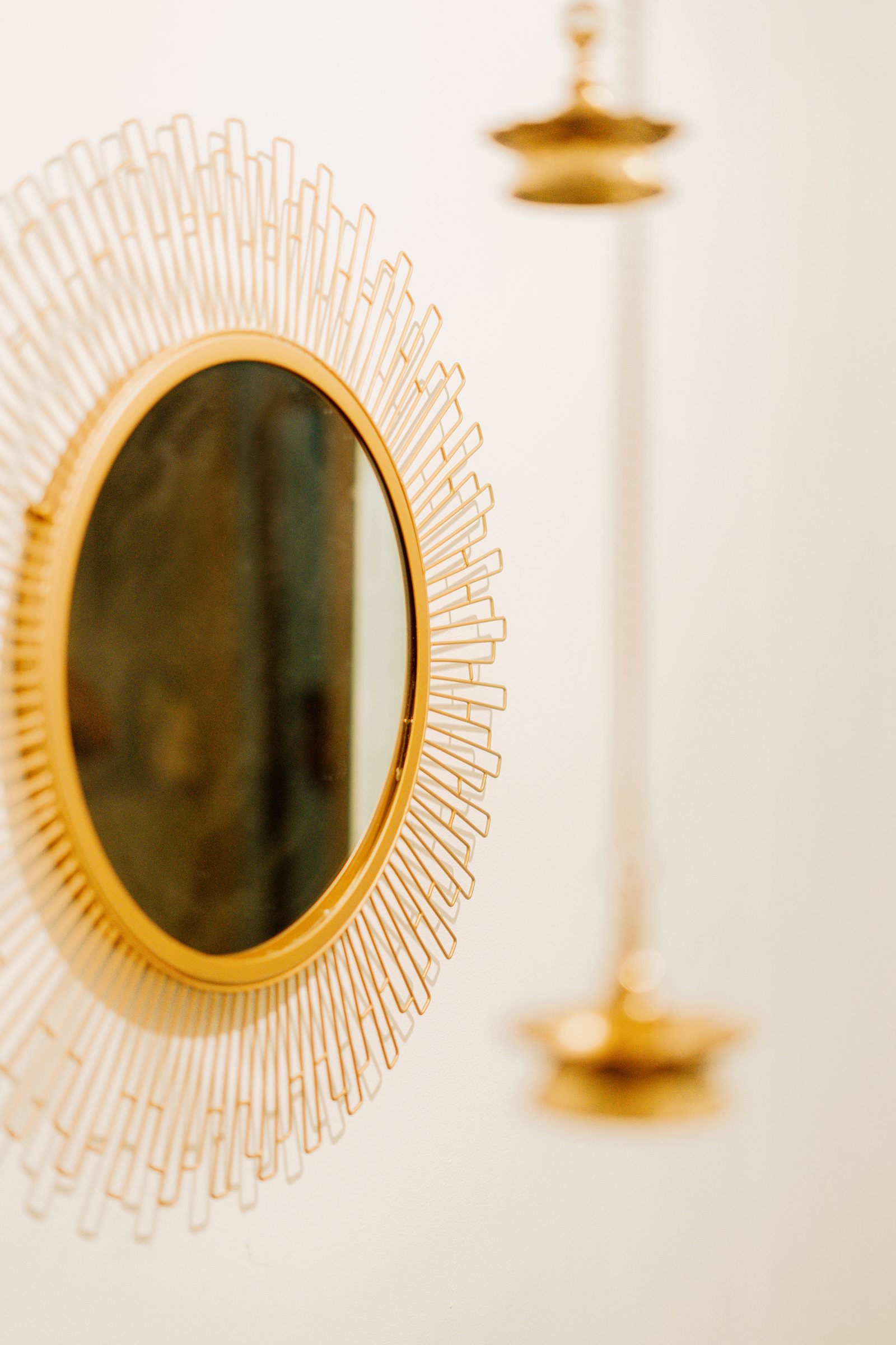 Side view of a round gold mirror and hanging brass oil lamp on a white wall
