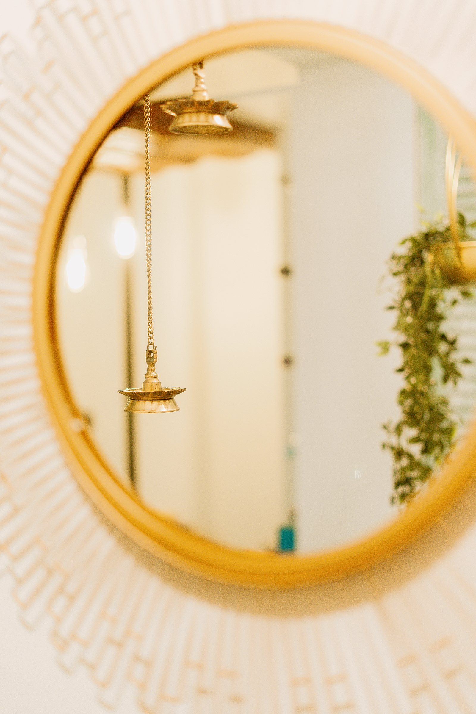 Round gold mirror reflecting a hanging brass oil lamp and softly lit hallway