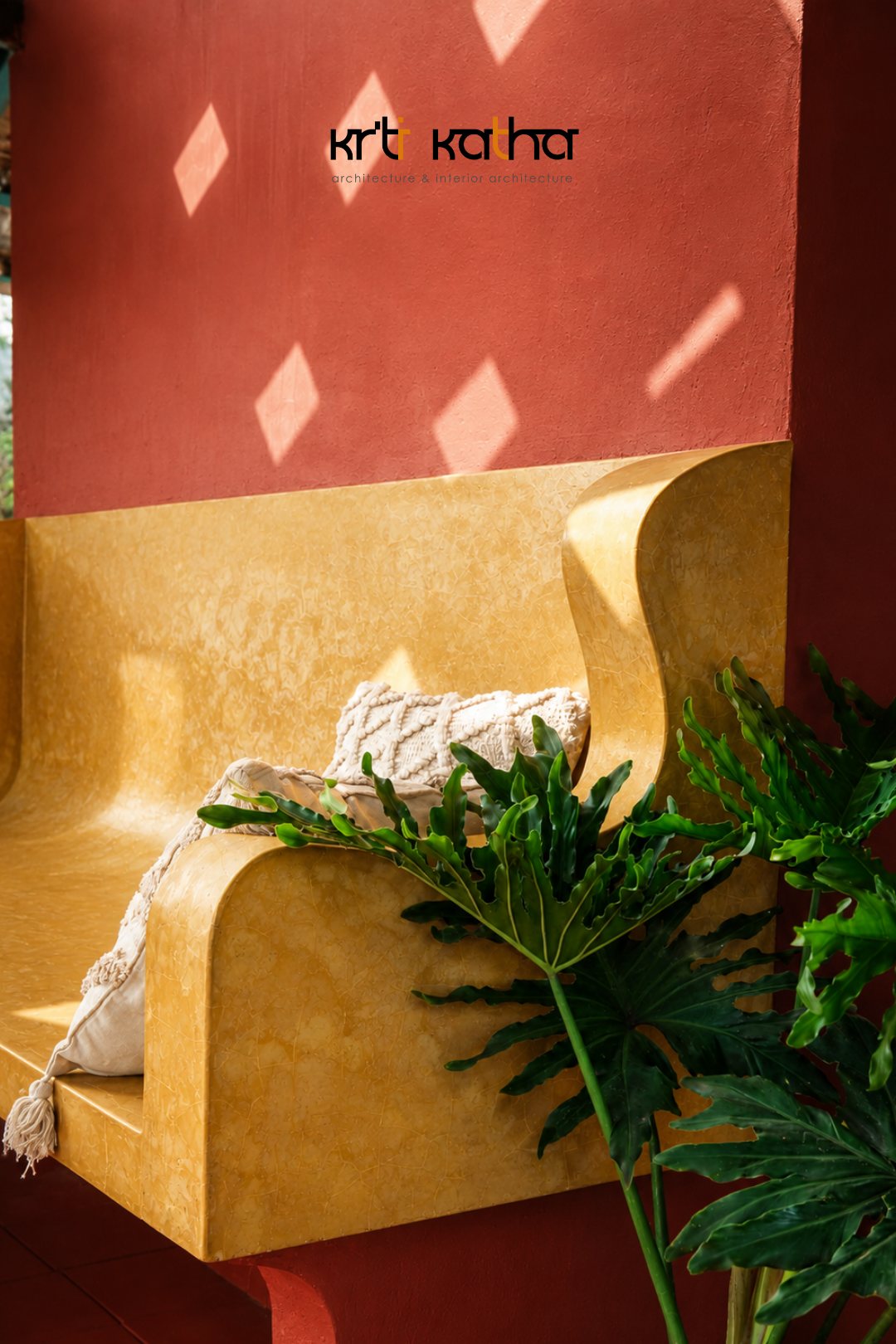 Sculpted ochre bench against a red wall, partly screened by large tropical leaves