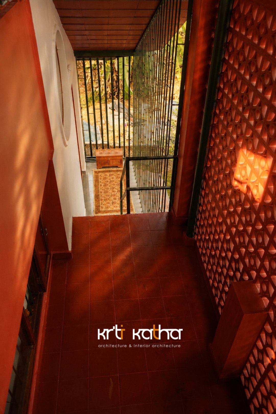 Red-tiled passage beside a perforated masonry wall, patterned by strong afternoon sunlight