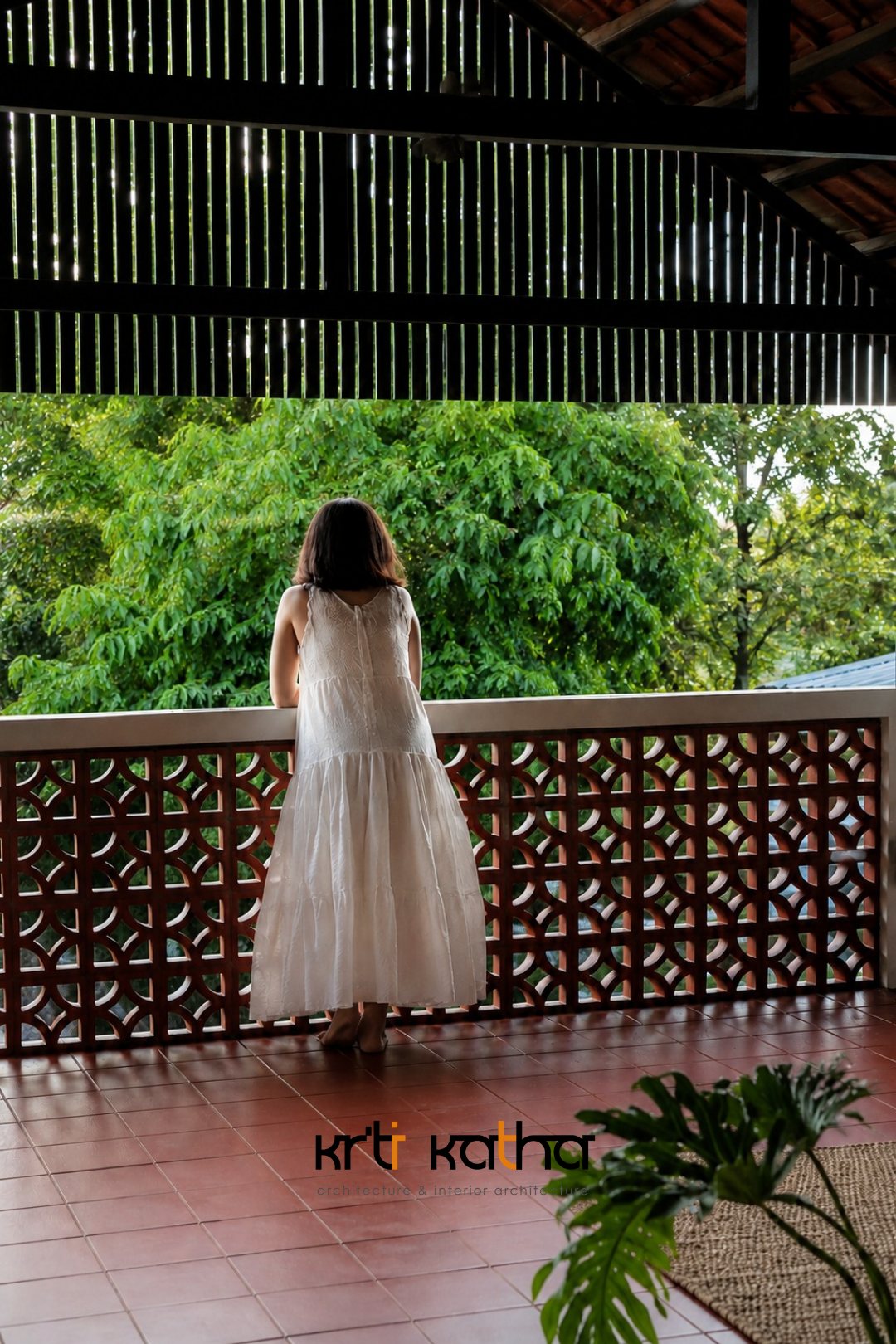 Woman in white facing dense greenery from a veranda with a patterned red balustrade