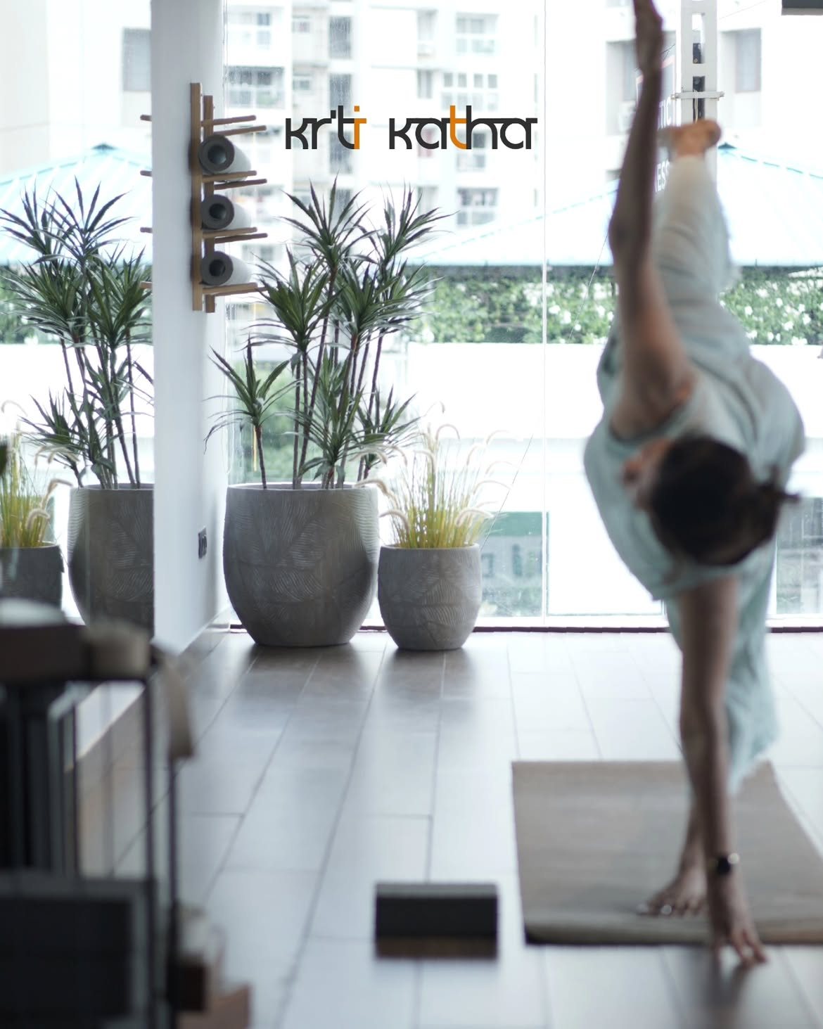Soft-focus view of a woman side-bending near a plant-lined studio window
